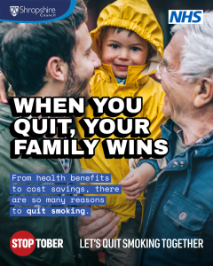 A toddler in in a yellow raincoat is being held by a man with dark hair and a beard. Nearby is an older man with white hair. They are all smiling.