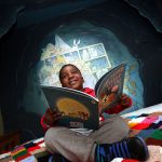 An image of a boy in the bear cave reading a children's book with a big smile on his face. Visit Bears at Shrewsbury Museum and Art Gallery from February to April 2019.