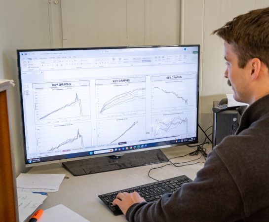 A man looking at a computer screen displaying graphs