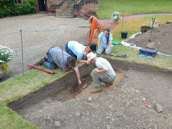 An image of the Shrewsbury Castle dig team discussing layers in part of the trench, trying to understand the relationships between different elements of the archaeology.