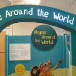 Image showing a blue archway into Rhyme Around the World exhibition with images of a fox with an umbrella, a lion leaping with two happy children and an antelope on its back and photos on the walls.