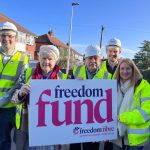 People posing with Freedom Fibre's Freedom Fund placard