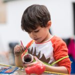 Little 4-year-old boy paints a pottery in the backyard of his house doing crafts and getting dirty. Realistic images with natural light