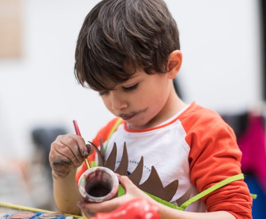 Little 4-year-old boy paints a pottery in the backyard of his house doing crafts and getting dirty. Realistic images with natural light