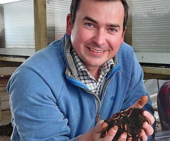 A man with his hands cupped holding soil with worms in it