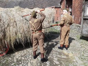 An image of two men in 1940's military dress prodding hay bails with rifles at the Wartime Farm event at Acton Scott Historic Working Farm. 