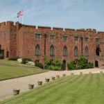An image of Shrewsbury Castle with the union jack flying at the left. There a lawns and plants that are in pristine condition on a beautiful summer day.