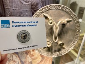 A silver coloured pin badge next to an artefact at Shrewsbury Museum