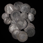 An image of the South Ludlow Hoard. The hoard consists of silver coins on a black background. The South Ludlow Hoard is now on display at Ludlow Museum at The Buttercross. The Hoards is owned by Shropshire Museums who are a service within Shropshire Council.