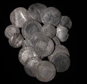 An image of the South Ludlow Coin Hoard. The hoard consists of silver coins on a black background. The South Ludlow Hoard is now on display at Ludlow Museum at The Buttercross. The Hoards is owned by Shropshire Museums who are a service within Shropshire Council. 