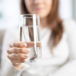 A woman in a white shirt holds a glass of water