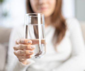 A woman in a white shirt holds a glass of water