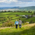 Image of two walkers on Bromlow Callow, Shropshire with bright skies, green fields and hedgrows.