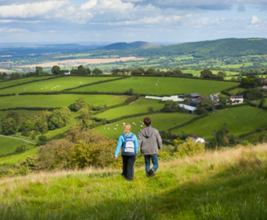 Image of two walkers on Bromlow Callow, Shropshire with bright skies, green fields and hedgrows.