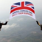 A picture of two members of a parachute display team holding the Armed Forces Flag in mid-air.