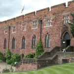 An image of Shrewsbury Castle showing the lush green lawns and flower sitting in the foreground of the medieval, earthworks castle.