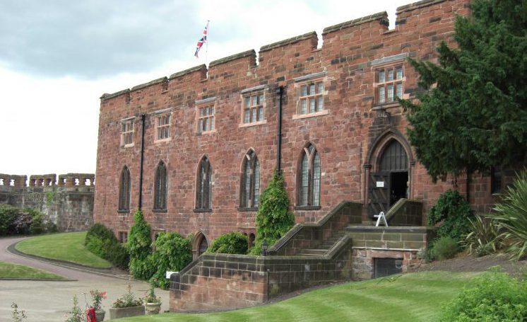 An image of Shrewsbury Castle showing the lush green lawns and flower sitting in the foreground of the medieval, earthworks castle.