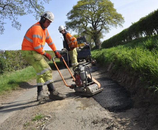 Two workmen carrying out find and fix pothole repairs on a country lane ear Adcote