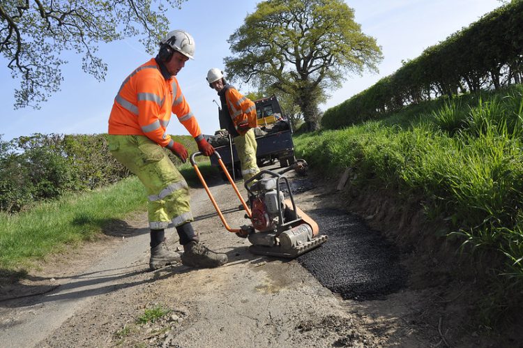 Two workmen carrying out find and fix pothole repairs on a country lane ear Adcote