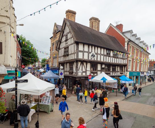 Oswestry town centre showing pedestrians walking round market stalls on the pavements