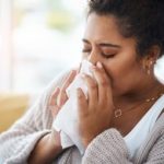 Woman sneezing. Flu and COVID-19 vaccines recommended