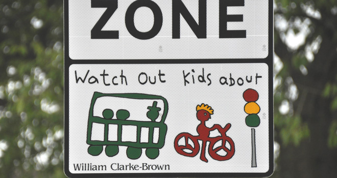 A picture of a road sign outside a school advising drivers to slow down.
