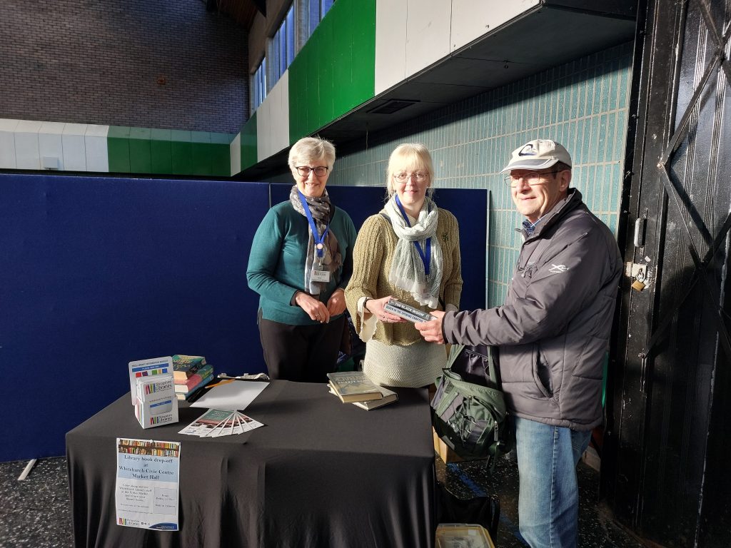 Whitchurch Library staff with a reader returning books on the market stall